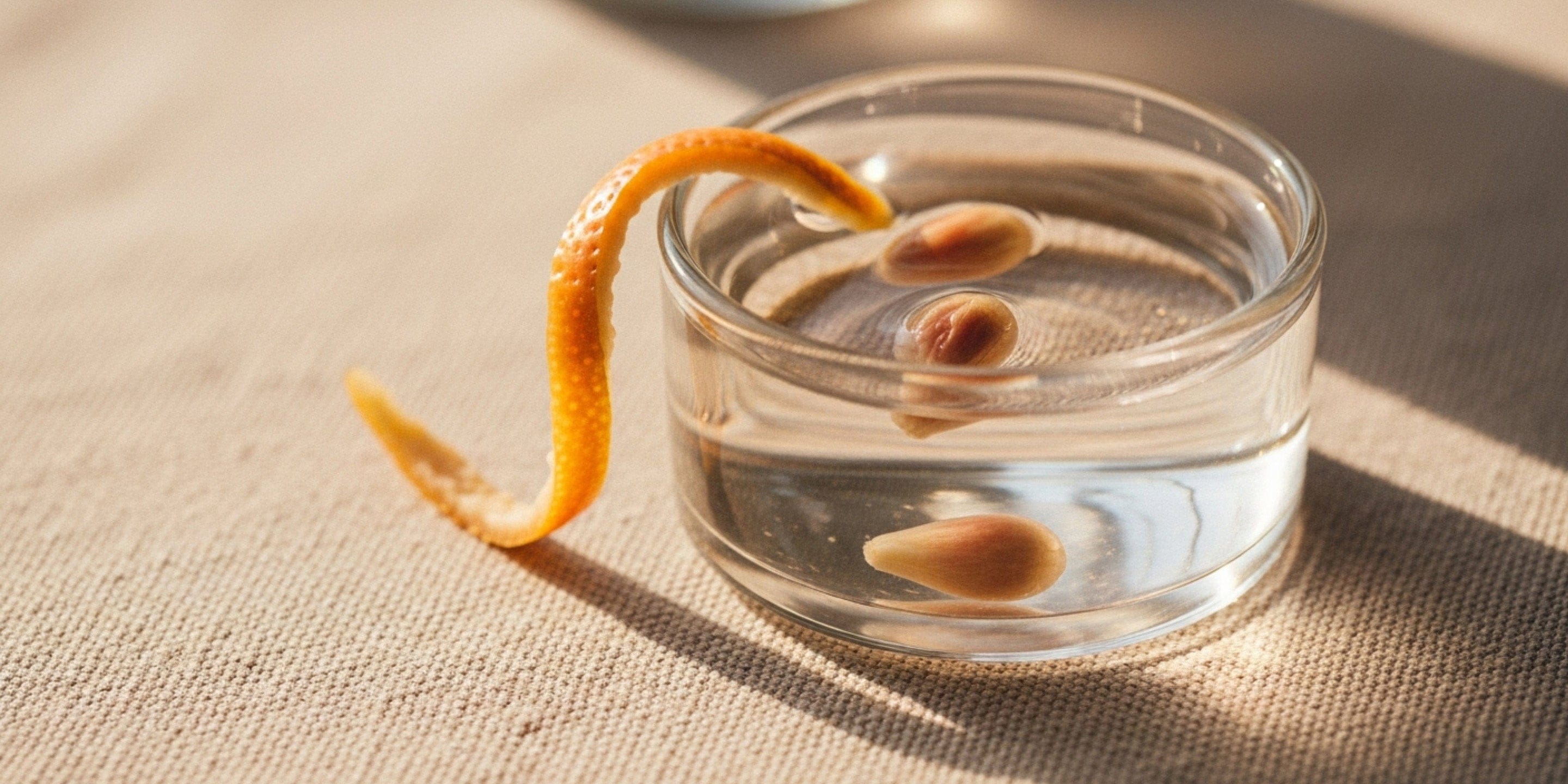 Glass container with seeds and an orange peel on a textured surface.
