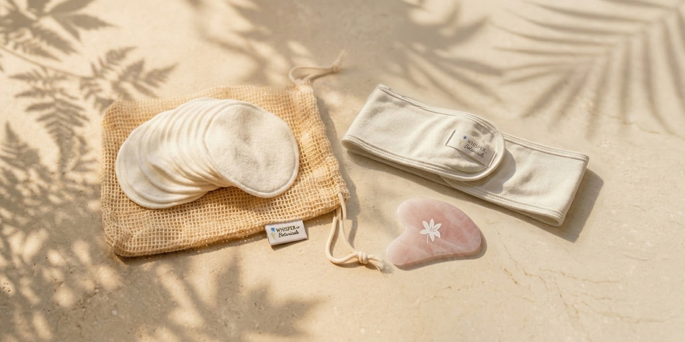 Set of reusable cotton pads, pouch, and heart-shaped stone on a sandy background with leaf shadows.