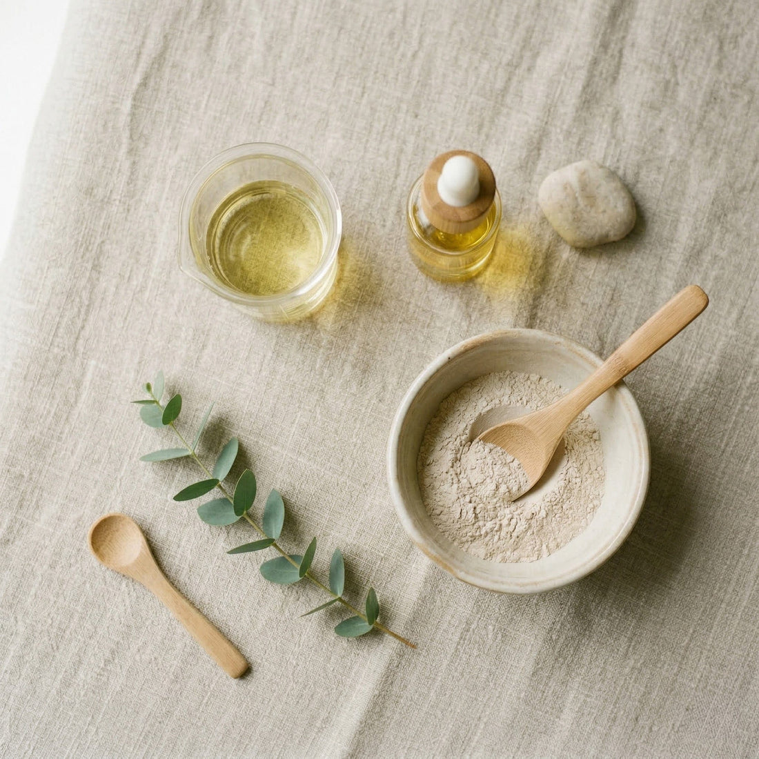 Bowl with powder, wooden spoon, and bottles on a textured surface.