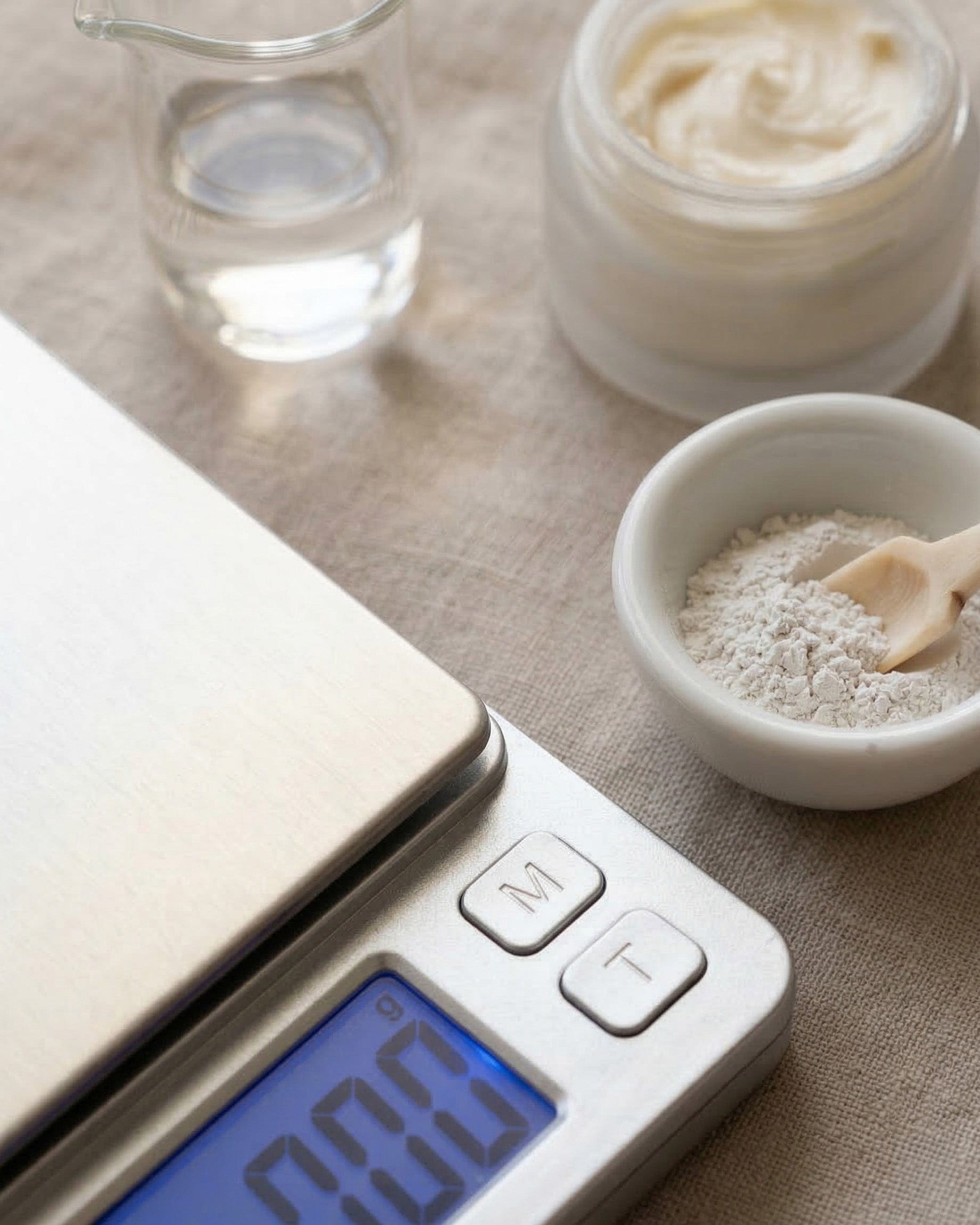 Digital kitchen scale with a bowl of clay and a glass container on a textured surface.