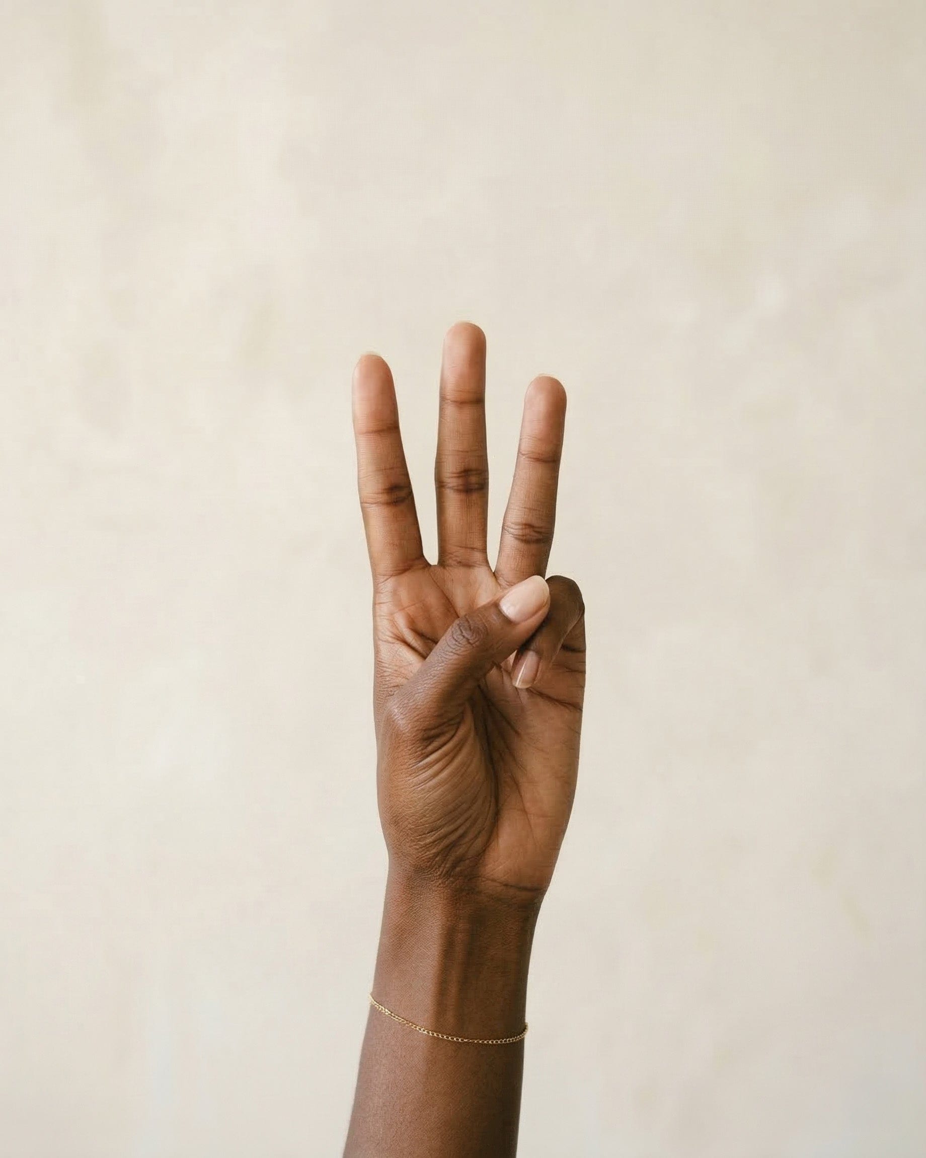 Hand with three fingers raised against a beige background.